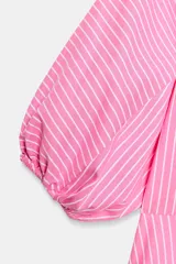 Camisa de popelín a rayas rosadas y blancas, con cuello solapa, mangas abullonadas por debajo del codo con terminación elástica, cintura entallada y bajo en evasé. Cierre frontal con botones ocultos.