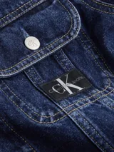 Campera de denim rígido color azul índigo oscuro, con corte cropped y ajuste auténtico de los 90. Presenta cuello en punta, bolsillos con solapa en el pecho y botones metálicos de la marca. Incluye una insignia con el logo de Calvin Klein en el bolsillo del pecho.