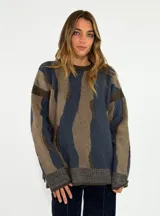 Sweater de tejido de punto con diseño abstracto de rayas irregulares en tonos azul y marrón. Presenta cuello redondo, mangas largas con caída de hombro y puños y ruedo acanalados.