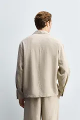 Camisa de corte relajado confeccionada en una mezcla de lyocell y lino. Presenta cuello bowling, manga larga con puño abotonado, bolsillo de plastrón en el pecho y cierre frontal con botones.