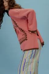 Buzo oversized de punto color tostado con diseño gráfico frontal en azul inspirado en una estampilla con una sirena y el texto 'Taormina'. Presenta tajos laterales, cuello redondo y terminaciones en contraste de color azul.