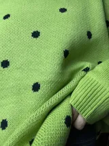 Suéter de tejido de punto color verde pistacho con diseño de lunares negros distribuidos por toda la prenda. Presenta cuello redondo y mangas largas abullonadas.