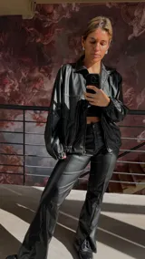 Campera bomber negra de cuero sintético con cierre frontal, cuello clásico y puños elásticos.