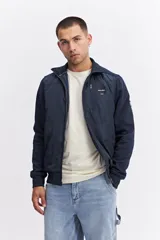 Campera de estilo deportivo con cierre frontal, confeccionada en una combinación de nylon y algodón. Presenta un diseño con paneles texturizados en las mangas, cuello alto y un parche decorativo con coordenadas en el pecho.