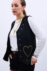 Chaleco negro con apliques de flores y tachas doradas en forma de corazón.