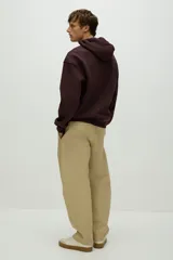 Campera con capucha de felpa color marrón oscuro (vino/borgoña), con interior cepillado suave. Presenta hombros caídos, cierre frontal, cordón para ajustar la capucha y bolsillos canguro delanteros. Puños y bajo terminados en punto acanalado.