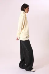 Buzo color crema con cuello alto abotonado y puños con ribete negro.