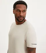 Remera deportiva de hombre con tecnología dry fit, cuello redondo y manga corta. Presenta un diseño liso en color beige con una pequeña etiqueta decorativa en el dobladillo.