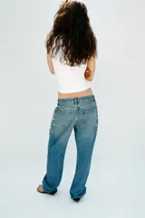 Jeans tiro medio de corte relaxed leg y largo completo, confeccionados en denim azul claro. Presentan detalles de aplicaciones de pedrería y joyas a contraste en los laterales superiores y bolsillos delanteros, estilo clásico de cinco bolsillos y cierre frontal con cremallera y botón metálico.