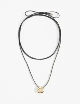 Collar de doble cordón negro ajustable mediante nudo en la parte superior, con un dije metálico liso de forma orgánica e irregular en tono dorado.