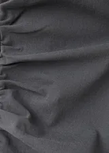 Vestido corto color gris oscuro, sin mangas y con cuello alto. Presenta un diseño entallado con panel fruncido en la cintura y falda asimétrica con volados.