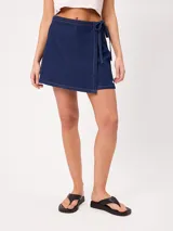 Falda corta de jean tipo pareo, con diseño cruzado para atar con tiras laterales, costuras pespunteadas a contratono y calce holgado.