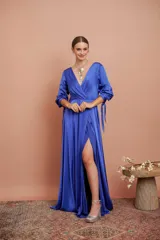 Vestido largo de satén color azul, con escote en V cruzado, mangas tres cuartos con detalles de lazos en los puños y falda larga con tajo frontal.
