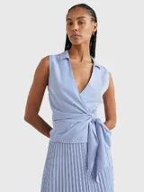 Blusa sin mangas con cuello camisero, diseño cruzado con lazo en la cintura y estampado a rayas verticales azules y blancas.
