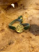 Pulsera con dije redondo dorado con diseño abstracto y cinta de terciopelo elástico color gris claro.