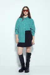 Camisa de silueta amplia y caída fluida, color celeste con rayas verticales blancas. Presenta cuello camisero clásico, cierre frontal con botones y un bolsillo aplicado en el pecho. Las costuras están resaltadas en azul oscuro.