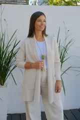 Saco abierto tipo cárdigan color crudo, de corte recto y largo medio, con mangas largas y dos bolsillos frontales aplicados.