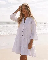 Vestido corto de lino natural color gris, con diseño amplio de capas, escote en V con botones frontales y mangas largas con volados en los puños.