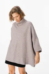 Sweater de tejido de punto suave en color beige, con silueta holgada, cuello alto y mangas tres cuartos con puños definidos.