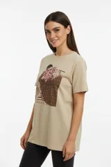 Remera de algodón color beige con cuello redondo y manga corta. Presenta un estampado artístico frontal con detalles de studs.