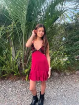 Vestido corto color bordó con escote en V, diseño de top triangular y aberturas laterales en la cintura. Presenta breteles finos cruzados en la espalda y falda con doble volado irregular en el ruedo.
