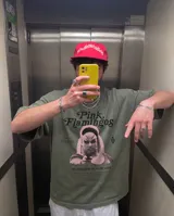 Remera de algodón con efecto lavado stone wash en color verde oliva. Presenta un diseño gráfico frontal inspirado en la película Pink Flamingos, con la imagen de Divine y tipografía estilo vintage.