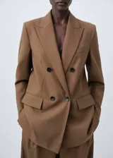 Blazer de corte recto y diseño estructurado, confeccionado en tejido mezcla de lana color marrón. Presenta cierre de doble botonadura, cuello con solapas de muesca, bolsillos de solapa en el frente y bolsillo de ribete en el pecho. Incluye forro interior y mangas largas con puños abotonados.
