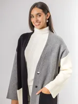 Sacón tipo tapado de corte largo, confeccionado en tejido de punto con diseño color block en tonos gris, negro y blanco. Presenta cierre frontal con botones, bolsillos laterales de parche y aberturas en los costados.