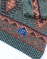Buzo tejido de punto con diseño geométrico de estilo étnico en tonos verde, marrón y salmón. Presenta cuello redondo, puños y ruedo acanalados, con etiqueta de la marca Denali en el interior y en el frente.