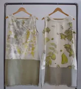 Vestido corto sin mangas, con estampado de hojas en tonos beige y verde, y falda color lila con detalle de flecos en el ruedo.