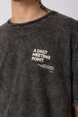 Remera negra con efecto acid wash, corte oversize y pequeño estampado tipográfico en el pecho con la frase 'A daily meeting point'.