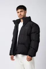 Campera puffer negra con diseño inflado, cuello alto y cierre frontal completo. Presenta logo bordado sutil en el pecho y puños ajustados.