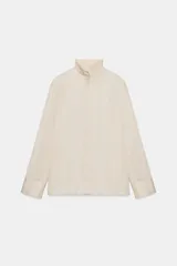 Camisa fluida de tejido satinado con cuello alto y manga larga terminada en puño ancho. Presenta cierre frontal con botones ocultos y bajo recto.