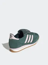 Zapatillas Adidas modelo SL 72 OG LT, de diseño retro inspirado en el running y el fútbol. Presentan un cuerpo de gamuza en color verde oscuro con las icónicas tres tiras laterales en tono rosado claro. Incluyen una lengüeta larga distintiva, entresuela blanca con detalles en rosa y suela de goma dentada color caramelo.