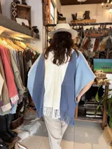 Ruana de hilo de algodón en tonos azul, celeste y crudo, con diseño en bloques de color, solapas en tono contrastante y flecos en el ruedo inferior.