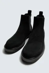 Bota estilo Chelsea de hombre, fabricada en piel con acabado de serraje. Presenta elásticos laterales, horma redonda y suela con ligero tacón.