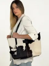 Cartera tote de cuero con pelo vacuno en tonos blanco y negro, con asas largas de hombro, parche frontal con logo y charms colgantes en forma de estrella y mini monedero.
