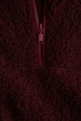 Buzo de sherpa con textura de borrego, color bordó, de corte oversized y hombros caídos. Presenta cuello elevado con medio cierre frontal, bolsillos laterales insertados y canesú en frente y espalda.