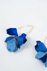 Aros colgantes con diseño de pétalos en color negro y azul oscuro, montados sobre un gancho de metal dorado.