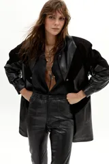 Chaqueta larga oversize de cuero y gamuza negra, con hombros marcados, cuello redondo y forro capitoneado.