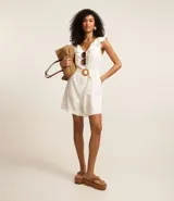 Enterito corto blanco sin mangas confeccionado en viscolino con escote V, espalda descotada con volados en el escote. Posee cinturón con hebilla redonda de ráfia y trabillas en la cintura.