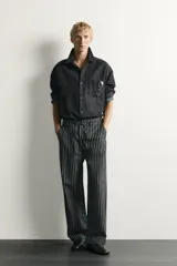 Pantalón relaxed fit de mezclilla con mezcla de algodón y lino, con diseño de rayas verticales oscuras y claras. Cuenta con cintura ajustable con cordón, bolsillos frontales, bolsillo cerillero y cierre frontal con cremallera y gancho metálico.