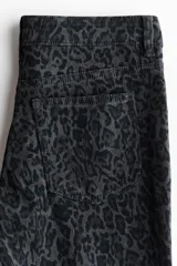 Jeans de tiro bajo con corte ajustado hasta el muslo y acampanado desde la rodilla. El tejido es de denim elástico con estampado de leopardo en tonos grises oscuros. Presenta cierre y botón, bolsillos delanteros decorativos y bolsillos abiertos traseros.