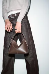 Bolso tipo mini shopper de estructura rígida en color crudo, con detalles de costuras en contraste y ribetes en color marrón oscuro. Cuenta con un asa de mano fija y cierre superior.