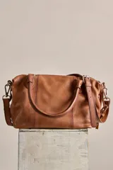 Cartera de cuero verde militar con acabado gastado, cuerpo blando, asas de mano, bolsillos frontales con cierre y tiras colgantes.