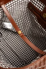Bolso tipo shopper color marrón de cuero sintético con diseño trenzado. Cuenta con doble asa de hombro y placa metálica con el logo de la marca en el frente.