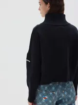 Polera de punto color negro con cuello alto, hombros caídos y mangas largas. Presenta puños, cuello y ruedo acanalados en tejido rib ancho.