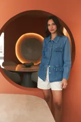 Campera de jean azul claro, con cuello camisero, botones frontales y detalles de volados en el pecho y la cintura. Tiene bolsillos funcionales en el pecho y la parte inferior.