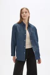 Sobrecamisa de jean azul índigo, con cuello clásico, cierre frontal con botones metálicos y dos bolsillos frontales tipo parche.