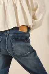 Jean de corte recto y tiro alto, confeccionado en denim azul con un lavado localizado que presenta efecto de bigotes y torceduras. Cuenta con cierre y botón frontal.